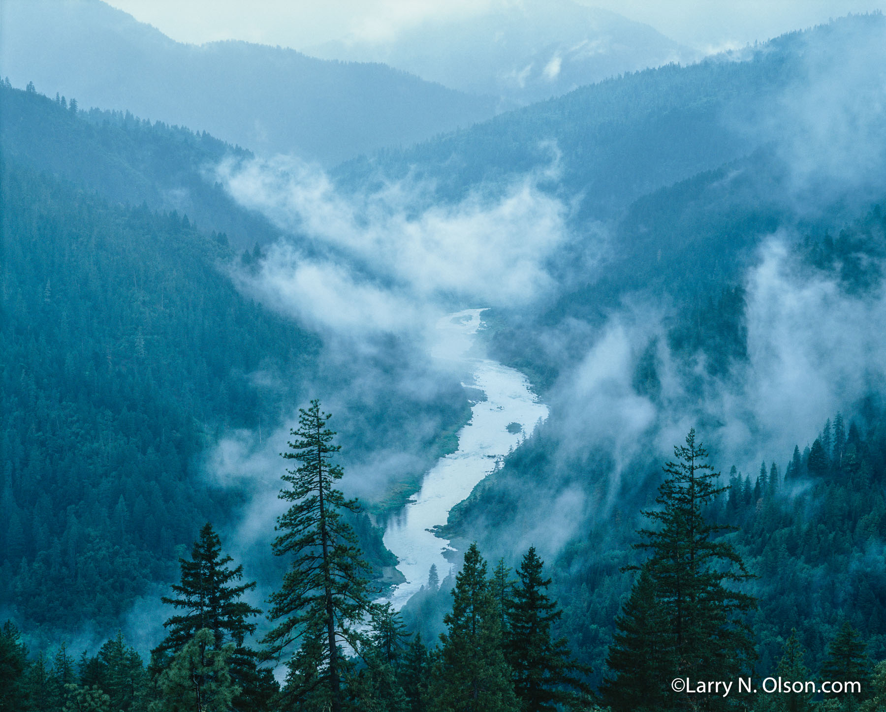 Rogue River, OR | A meandering river flows through a  forested valley with low lying clouds.