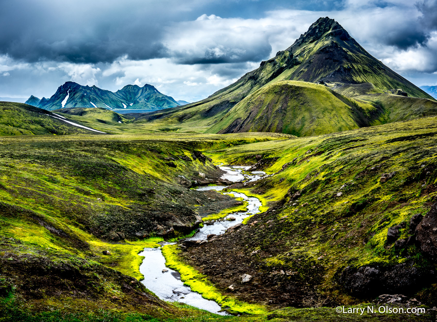 Landmannalaugar, Iceland | A river runs underneath volcanic peaks on the Landmannalaugar, Iceland. Interesting shapes of the mountains make hiking the Landmannalaugar in Iceland very unique.