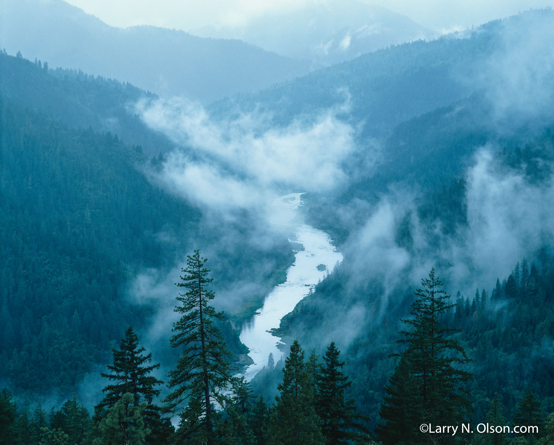 Rogue River, OR | A meandering river flows through a  forested valley with low lying clouds.