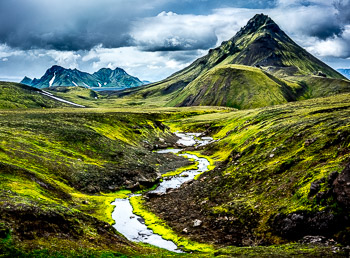 Landmannalaugar, Iceland | A river runs underneath volcanic peaks on the Landmannalaugar, Iceland. Interesting shapes of the mountains make hiking the Landmannalaugar in Iceland very unique.